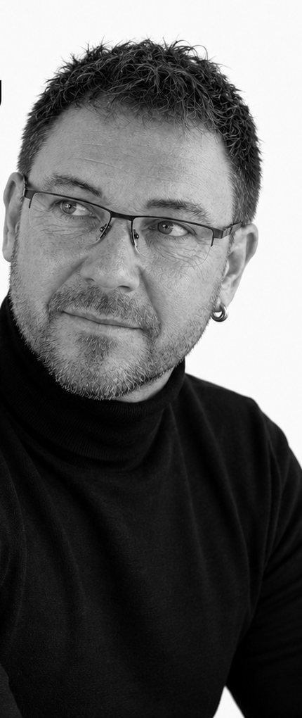 Alex im schwarzen Rollkragenpullover, schaut lächelnd zur Seite